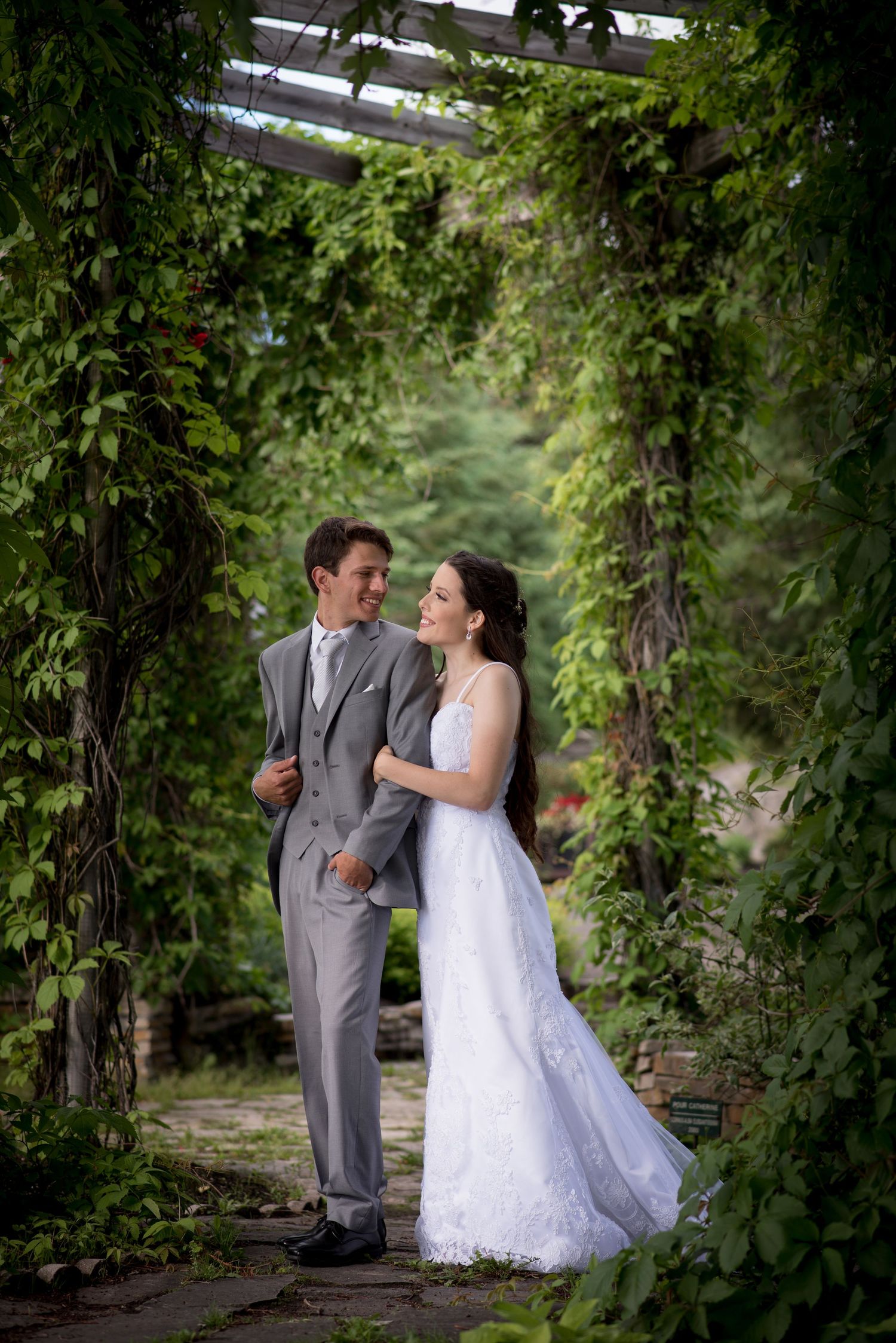 A couple shares a romantic moment under a vine-covered garden archway on their wedding day.