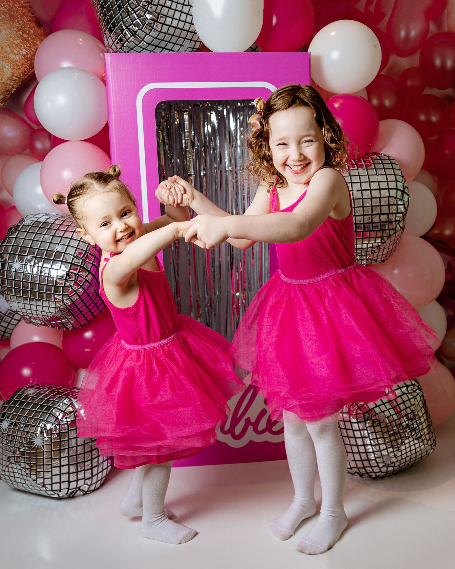 Two dancers in matching hot pink tulle dresses perform together against a backdrop of silver disco balls and white balloons.