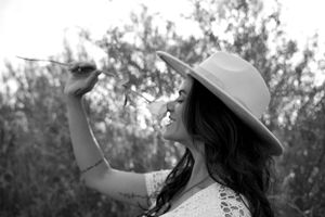 Artistic black and white portrait of someone in a hat blowing dandelion seeds.