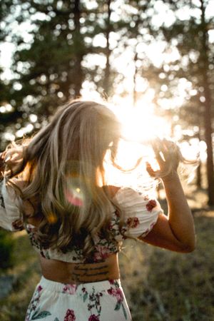 Silhouette of a person in a floral dress dancing in golden sunset light through pine trees.