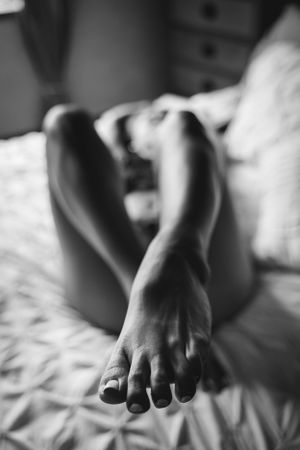 Black and white close-up of bare feet and legs resting on soft bedding.