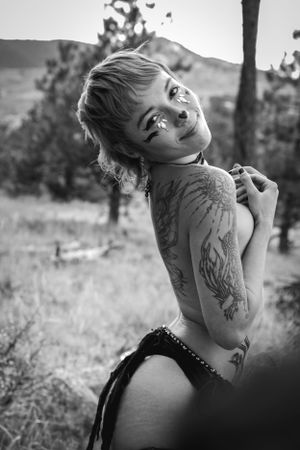 Black and white outdoor portrait showing tattoo art and playful expression in natural setting.