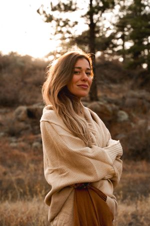 Person wearing cozy sweater poses in warm sunset light against mountain landscape.