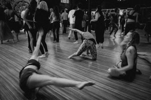 Black and white photo of people dancing on a wooden floor at a social gathering.