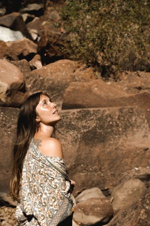A woman in a floral wrap gazes upward while posing against red rock formations in sunlight.