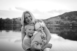 A tender family moment captured in black and white by a serene lake with mountains in background.