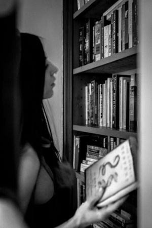 Black and white photo of someone browsing books on a shelf in dim lighting.