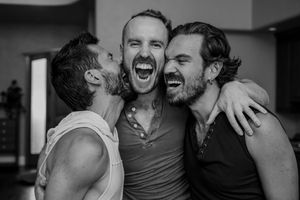 Black and white photo showing three friends laughing and embracing in a joyful candid moment.