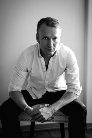 Portrait of person in white button-down shirt sitting on upholstered chair.