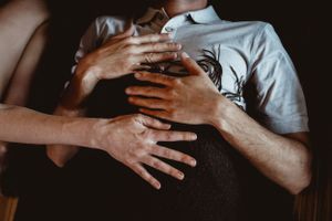 Intimate artistic photo of hands touching and embracing in dramatic lighting.