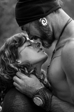 Black and white intimate portrait showing passionate embrace between bearded man in beanie and curly haired woman.