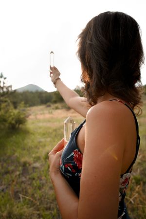 Silhouette holding crystal in sunlit mountain landscape during golden hour.