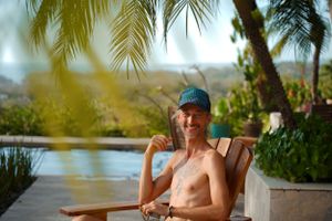 Person relaxing in a chair by a tropical pool with palm trees in the background.