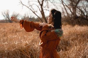 Person in rust colored dress twirling joyfully in autumn field at sunset.
