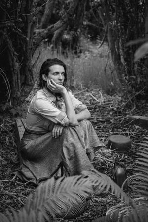 Vintage-style black and white portrait of someone sitting thoughtfully in a forest setting.