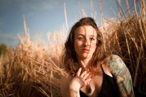 Portrait of tattooed woman in natural lighting amid tall grasses at golden hour.