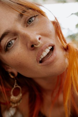 Close up portrait with vibrant orange hair, septum piercing and bohemian jewelry.
