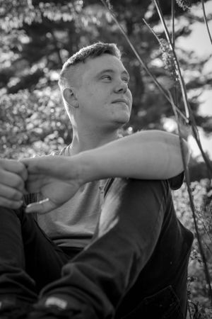 Artistic black and white portrait of someone sitting outdoors in natural lighting and looking upward.