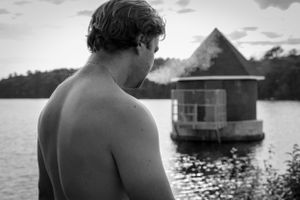 Silhouette of a figure gazing at a floating house on a tranquil lake.