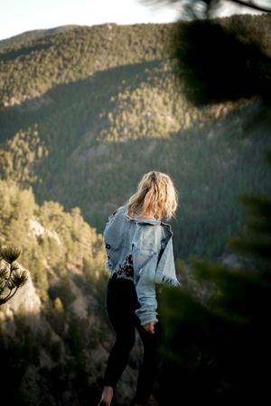 Person in denim jacket overlooking mountain landscape at sunset.