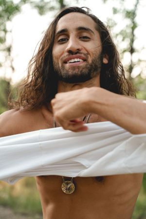 A person with long dark hair and necklace adjusts white fabric outdoors.