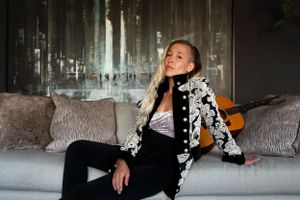 Stylish figure in black and white embroidered jacket relaxes on gray couch.