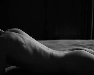 Artistic black and white nude study showing curved lines of back in low light.