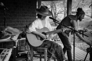 Musicians performing on acoustic guitars in black and white on a porch.
