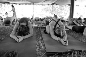Two people lie in relaxing poses on yoga mats during a wellness retreat under a tent canopy.