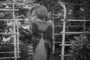 Black and white portrait showing back of dress with detailed wing design in outdoor garden setting.