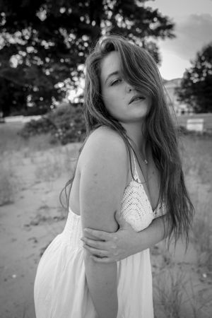 Black and white portrait of someone in a white dress posed outdoors in natural lighting.