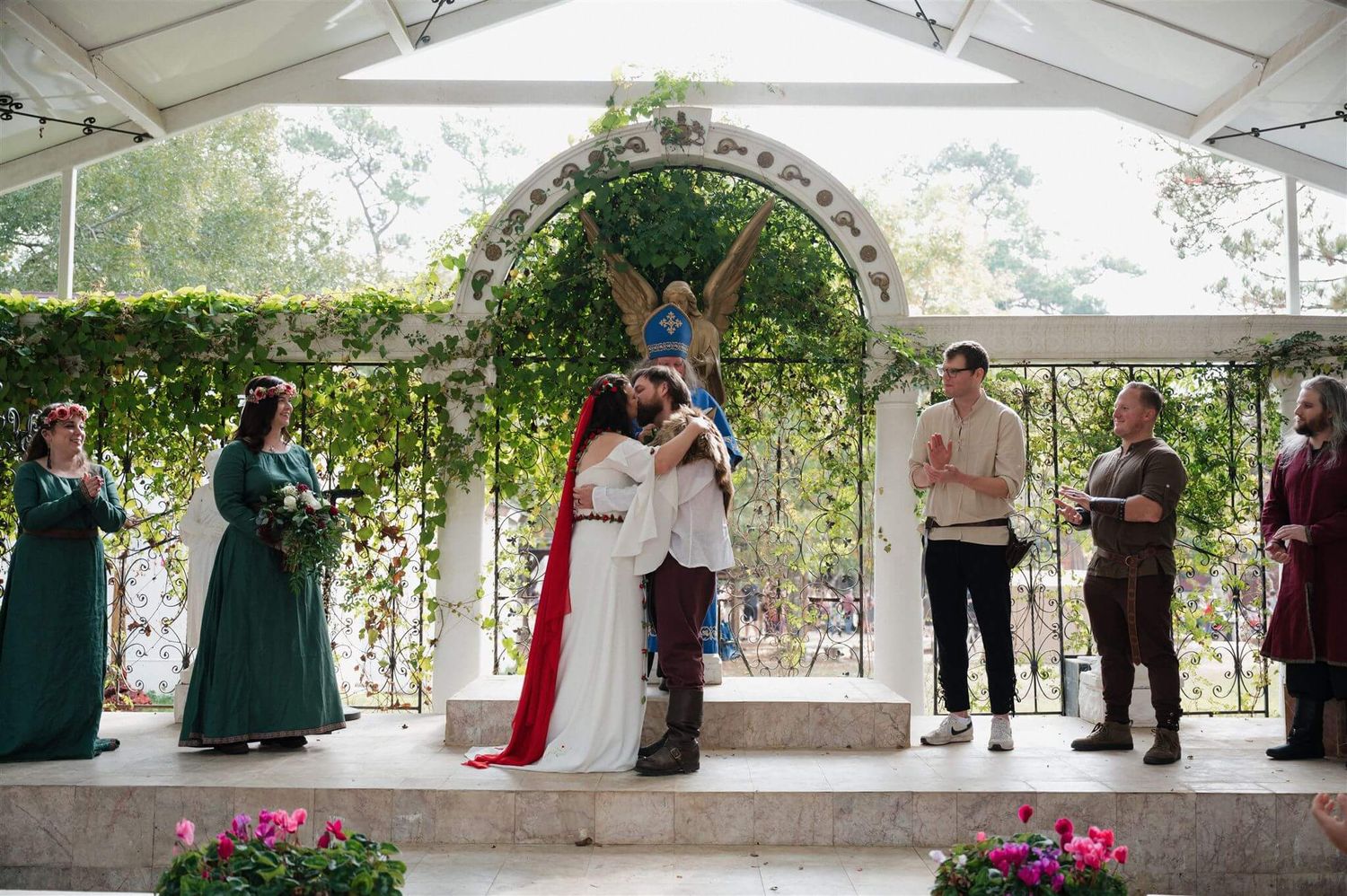 A wedding celebration under a decorated archway with guests in medieval attire and green dresses.