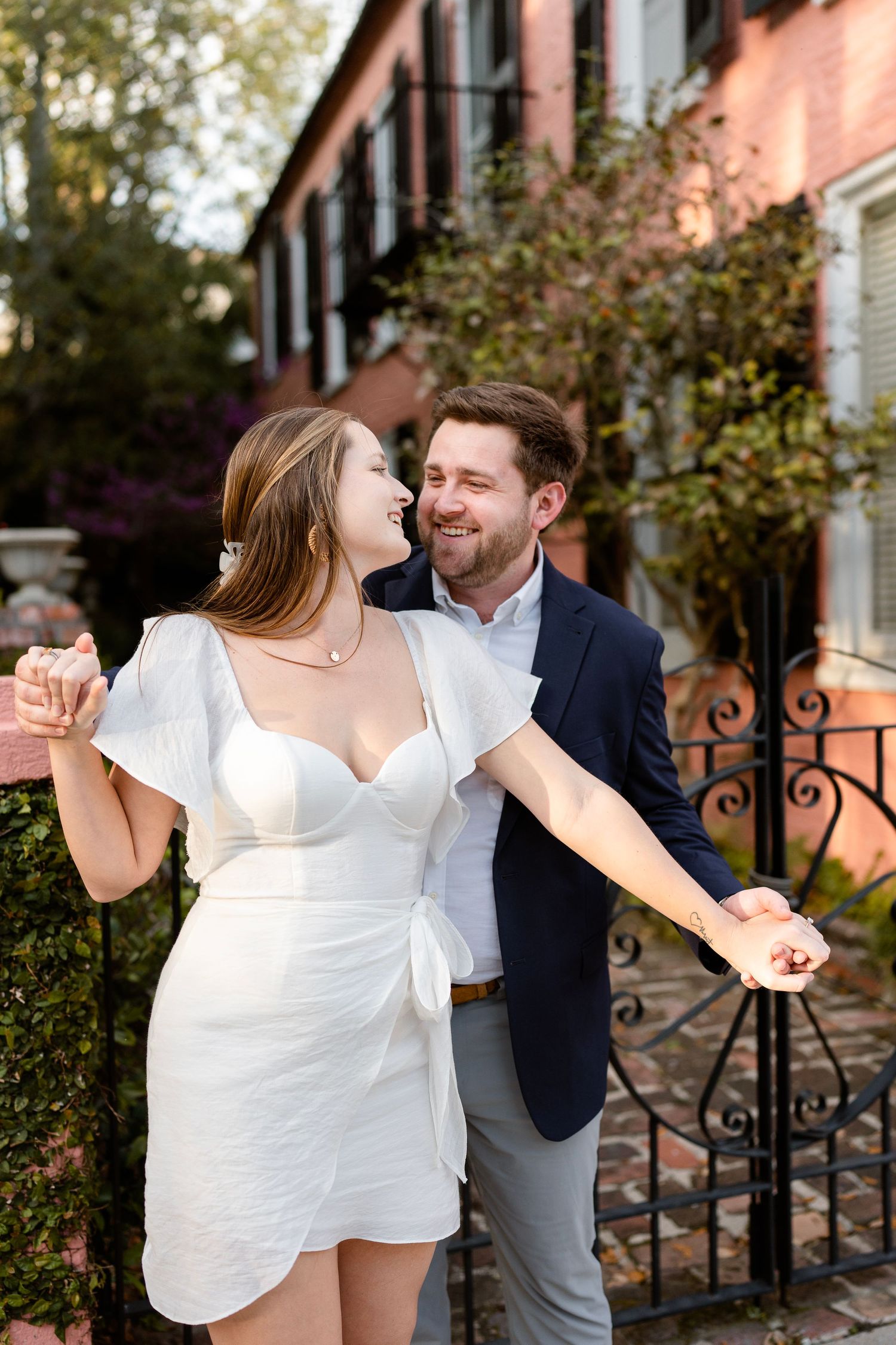 A joyful couple dancing together on a charming cobblestone street in front of a pink building.