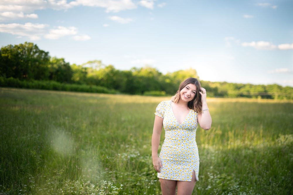 A person in a white dress stands in a sunny meadow during golden hour.