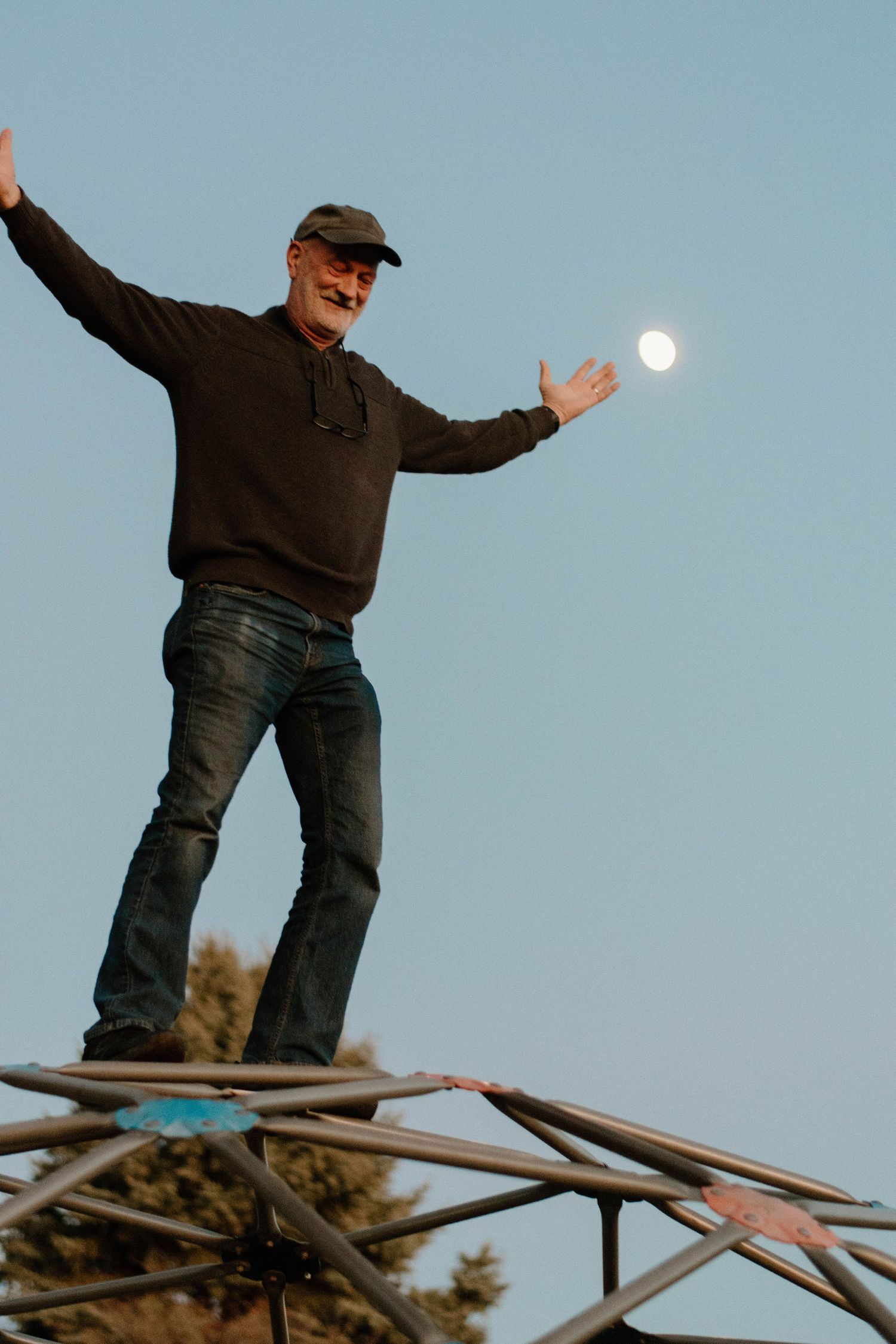 Person poses dramatically with moon appearing to float between outstretched hands.