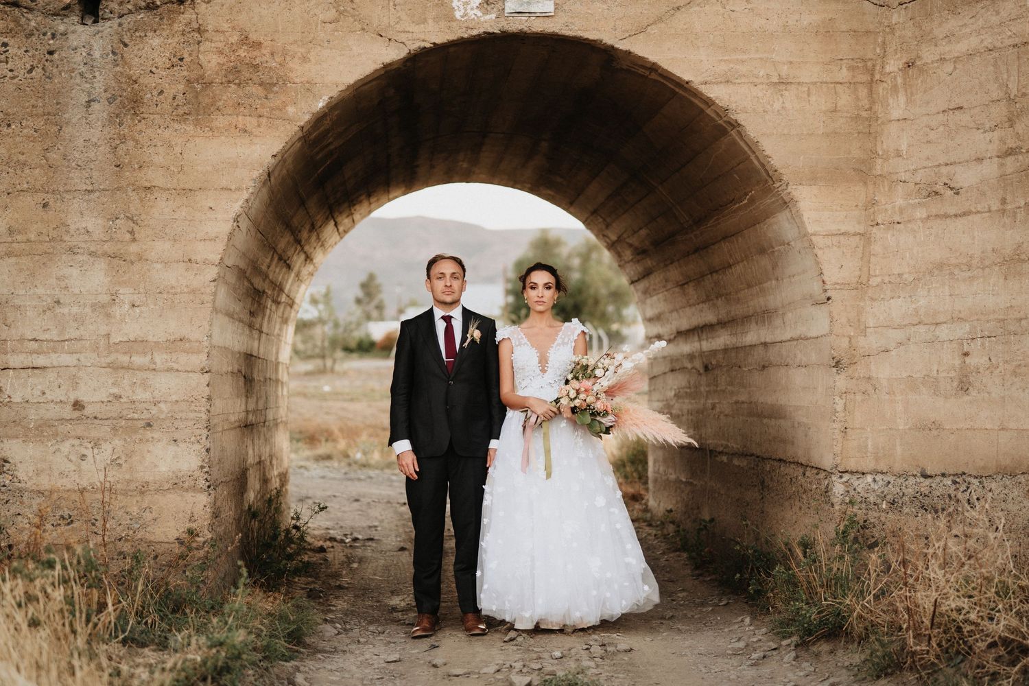 A wedding photo captured under a stone archway tunnel with natural lighting.