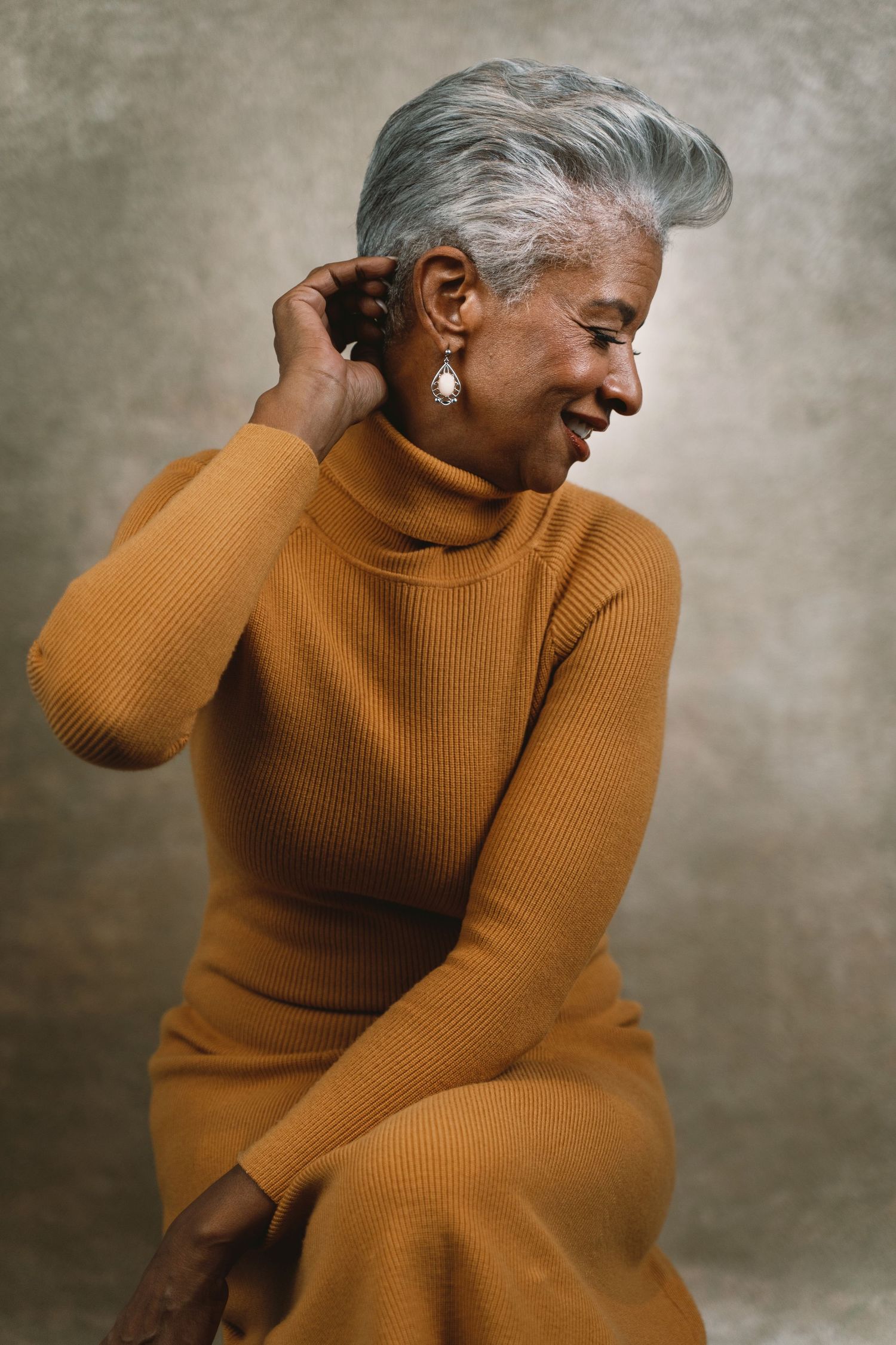 Elegant older woman in mustard turtleneck dress smiling in studio portrait.