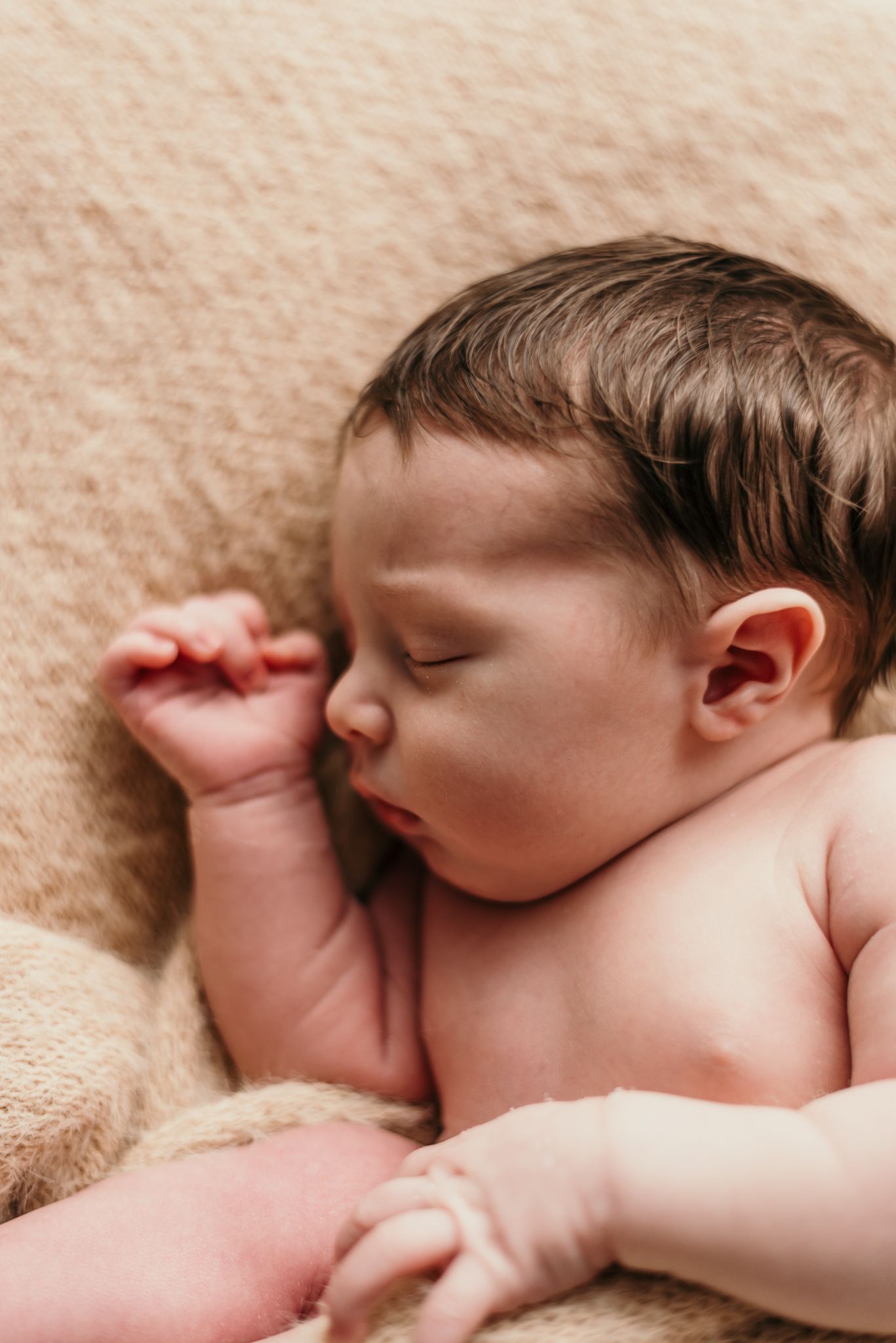 Close-up portrait of sleeping newborn with tiny fist raised near face.