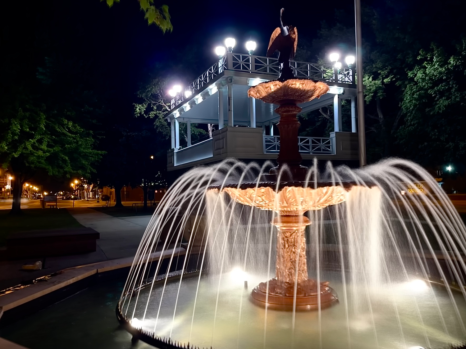 Illuminated fountain with cascading water streams at night in a park setting.