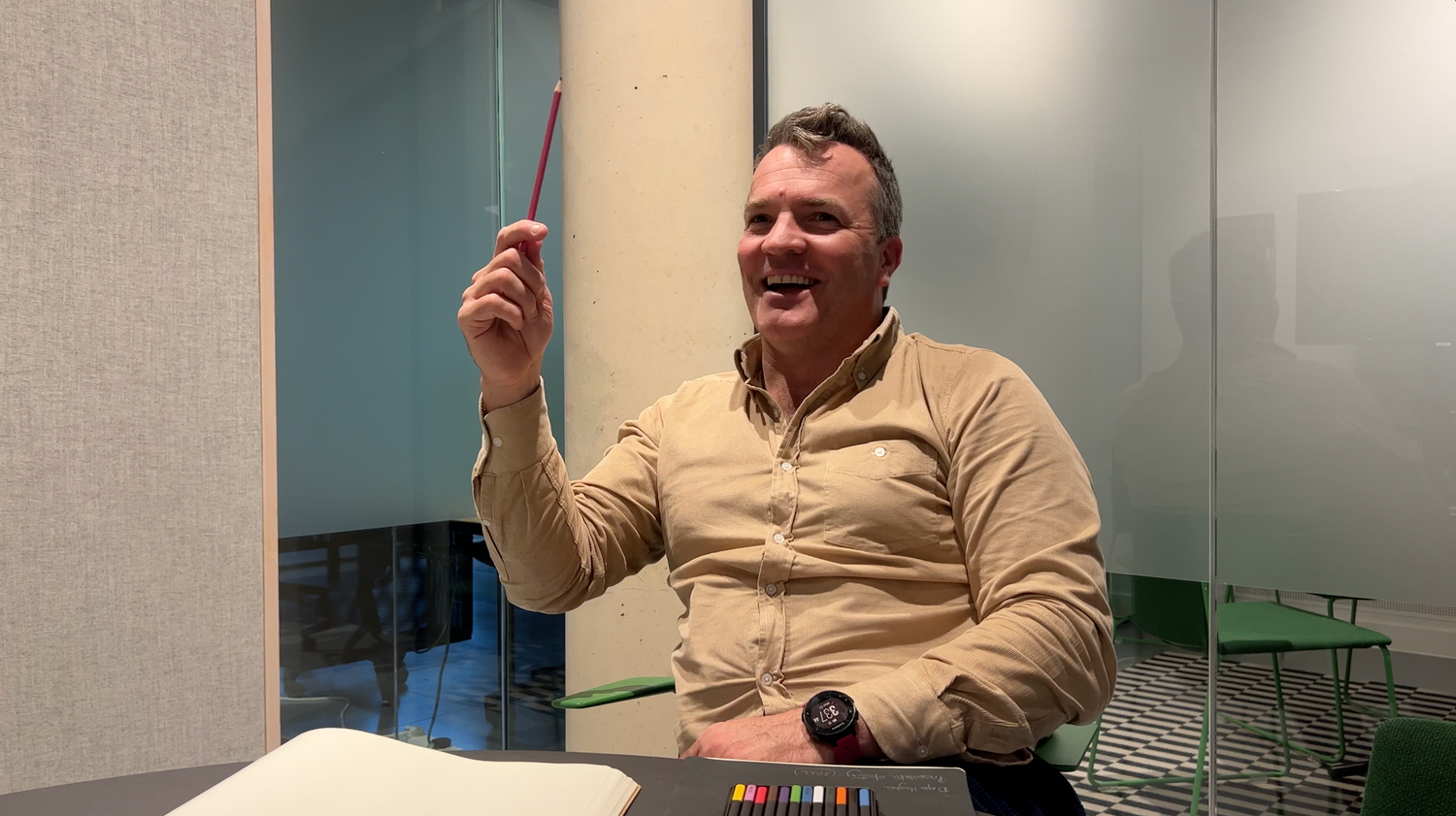 mature man having an interview in a room holding a pencil in his hand and wearing a beige shirt