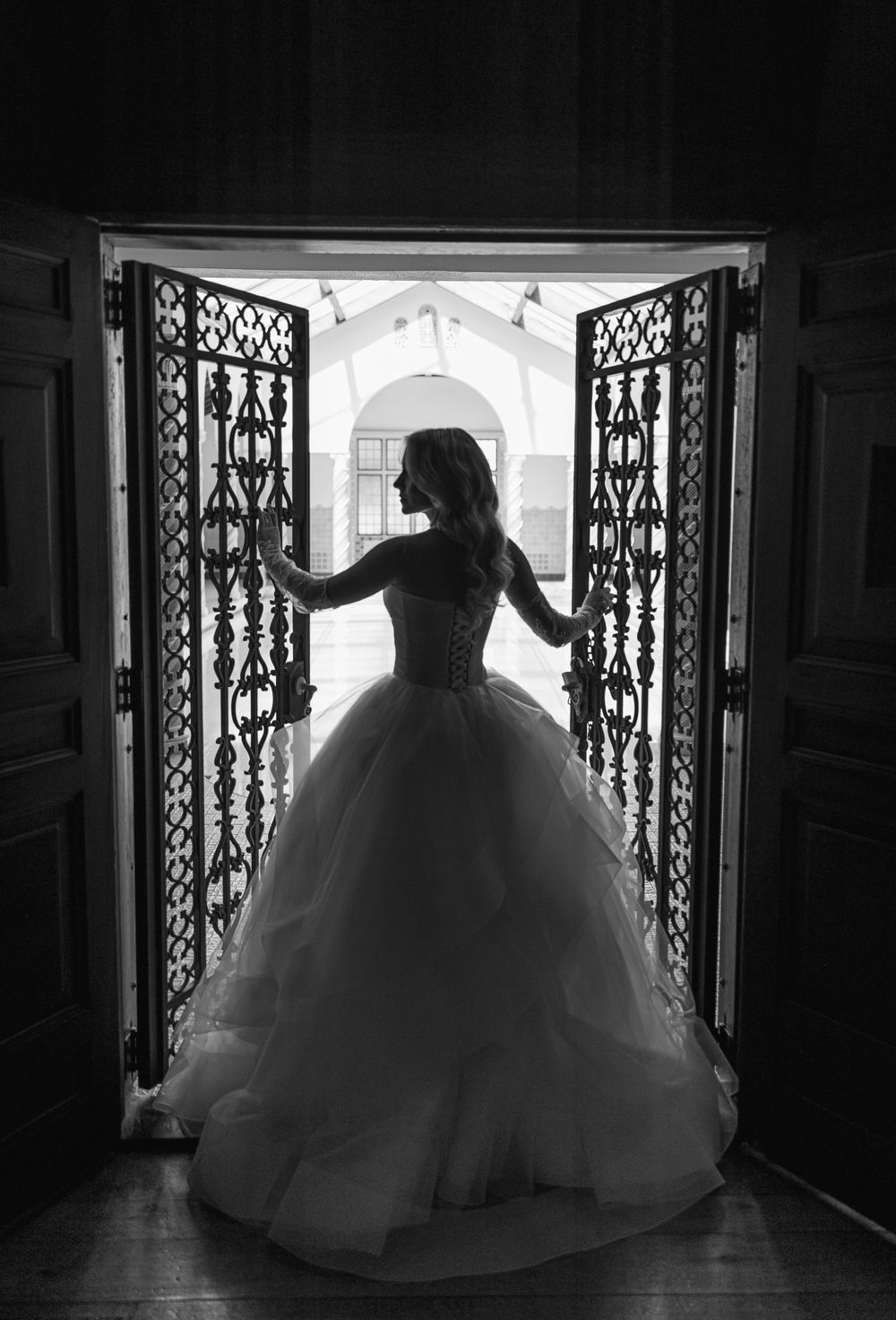 Silhouette of bride in ballgown standing between ornate iron gates.