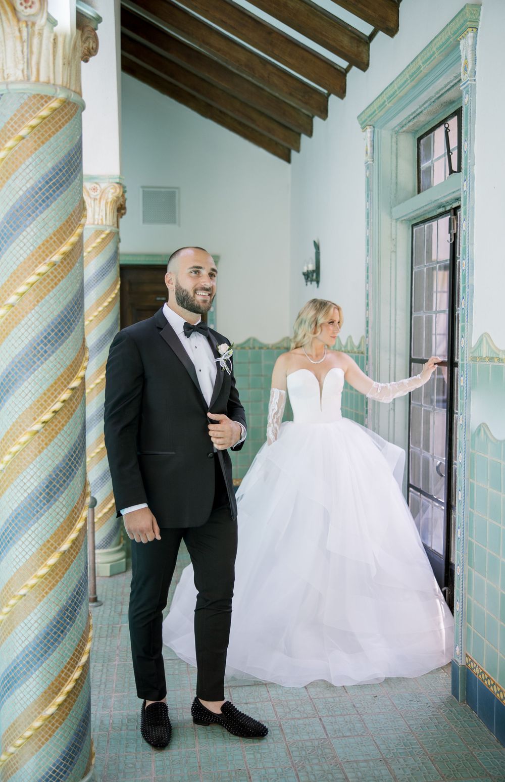 Wedding couple poses by decorative columns and mint green doorway in elegant venue.