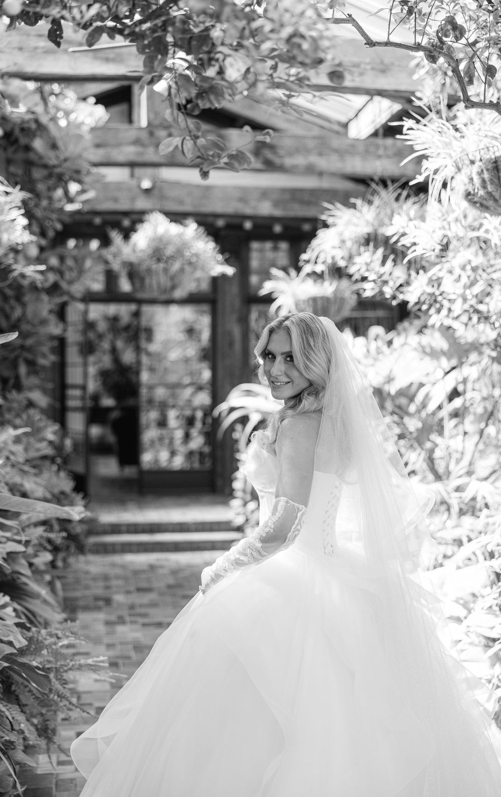 A dreamy black and white bridal portrait in a lush garden setting with architectural details.