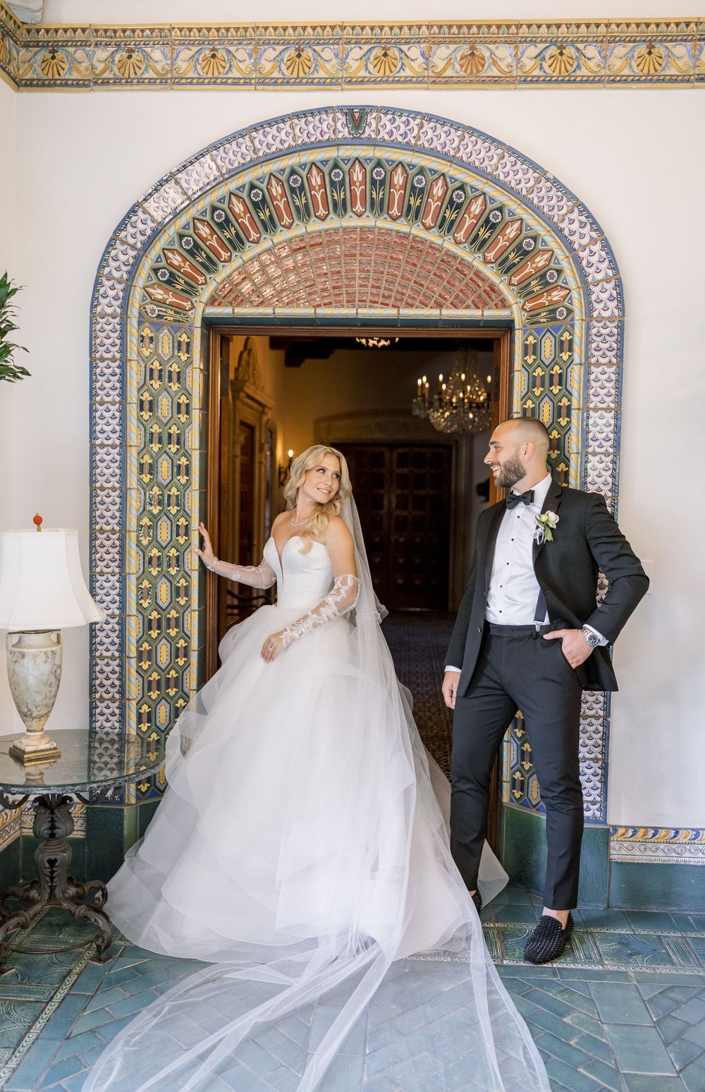 A wedding couple poses in front of a beautifully tiled Moorish archway in an elegant venue.