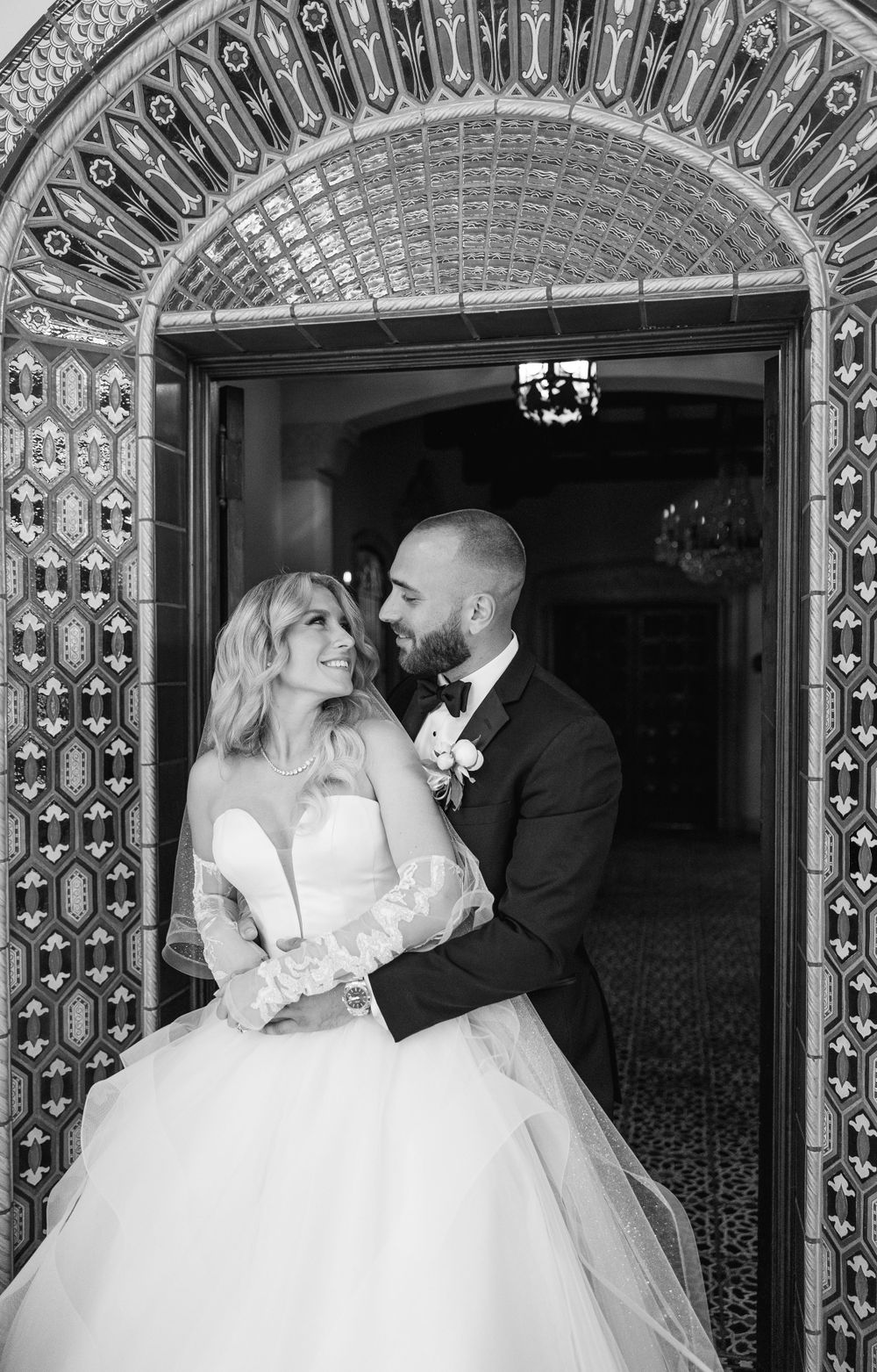 A romantic black and white wedding portrait under an ornate tiled archway.