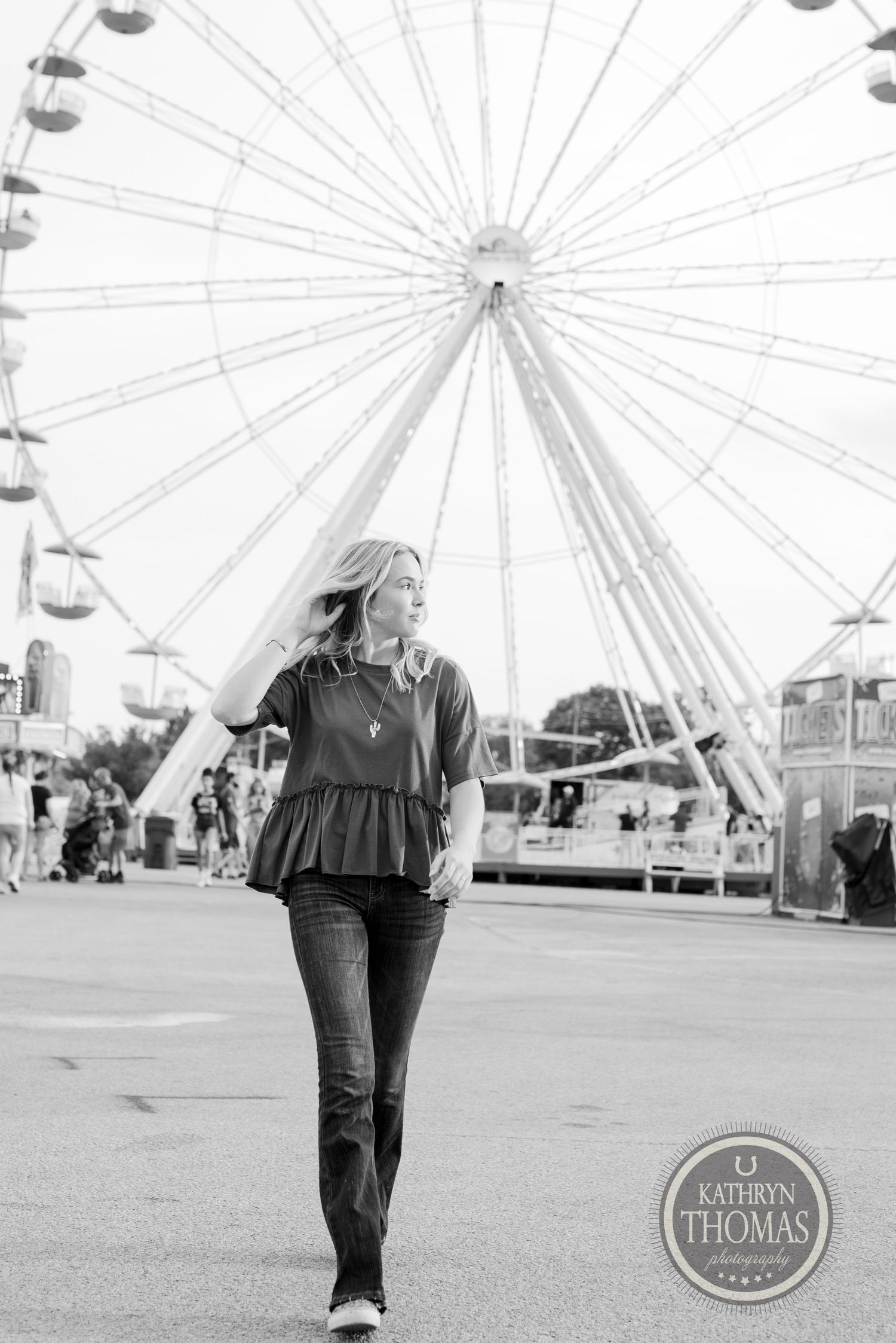 Black and white portrait of someone walking past a carnival ferris wheel.