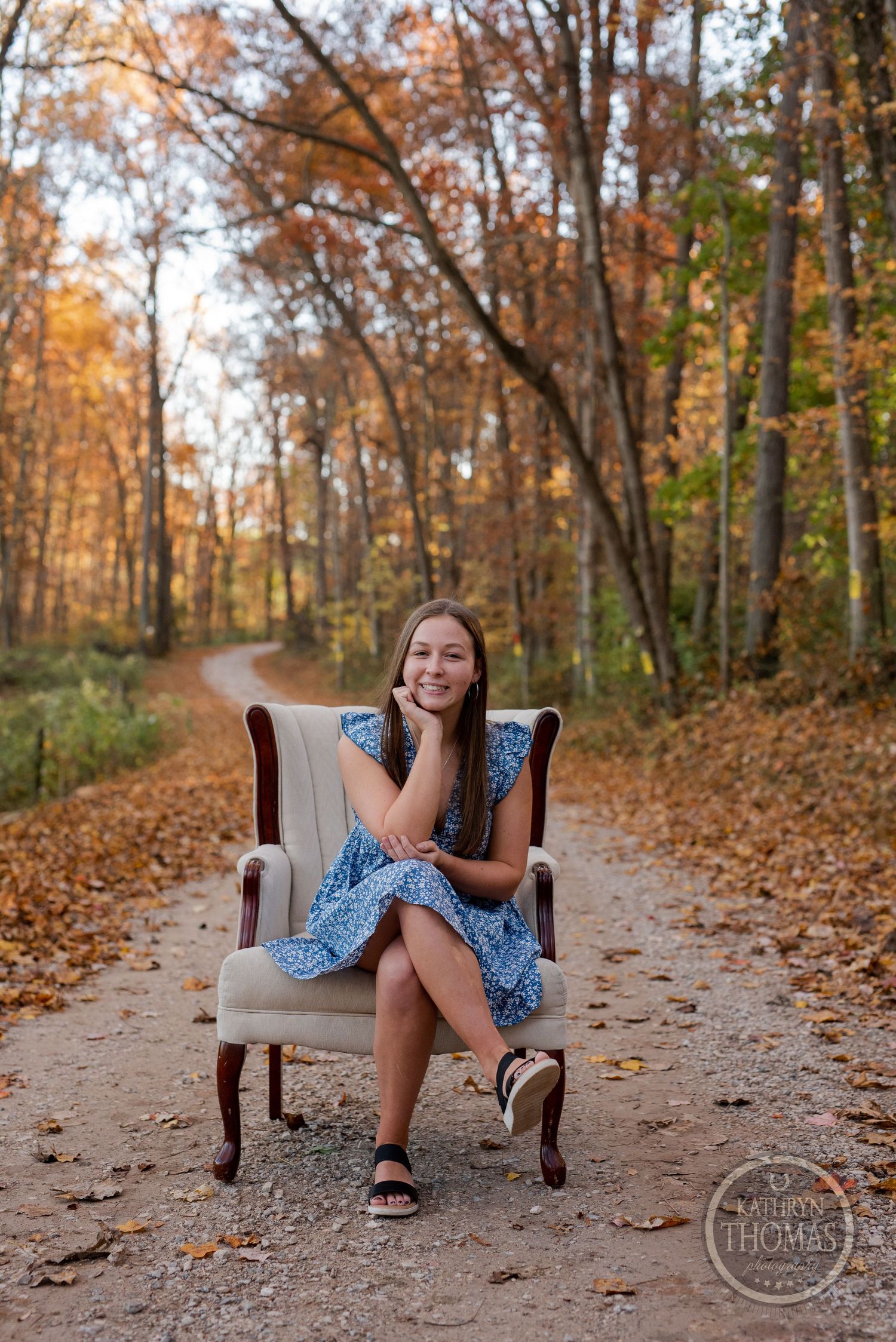 A vintage armchair placed on a forest path with autumn leaves creating a cozy outdoor setting.
