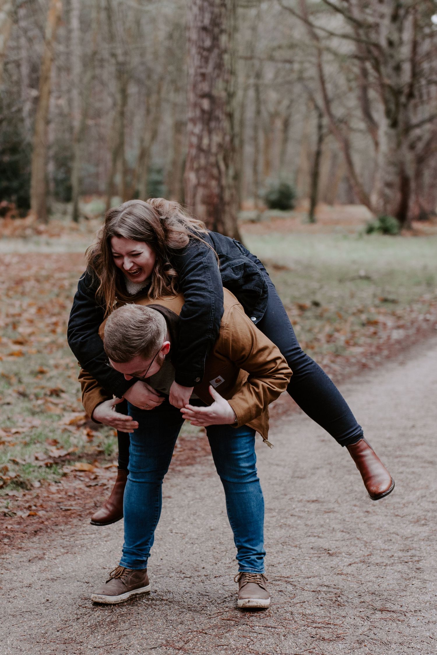 a couple are attempting a piggy back. the lady is falling off and they are both laughing.
