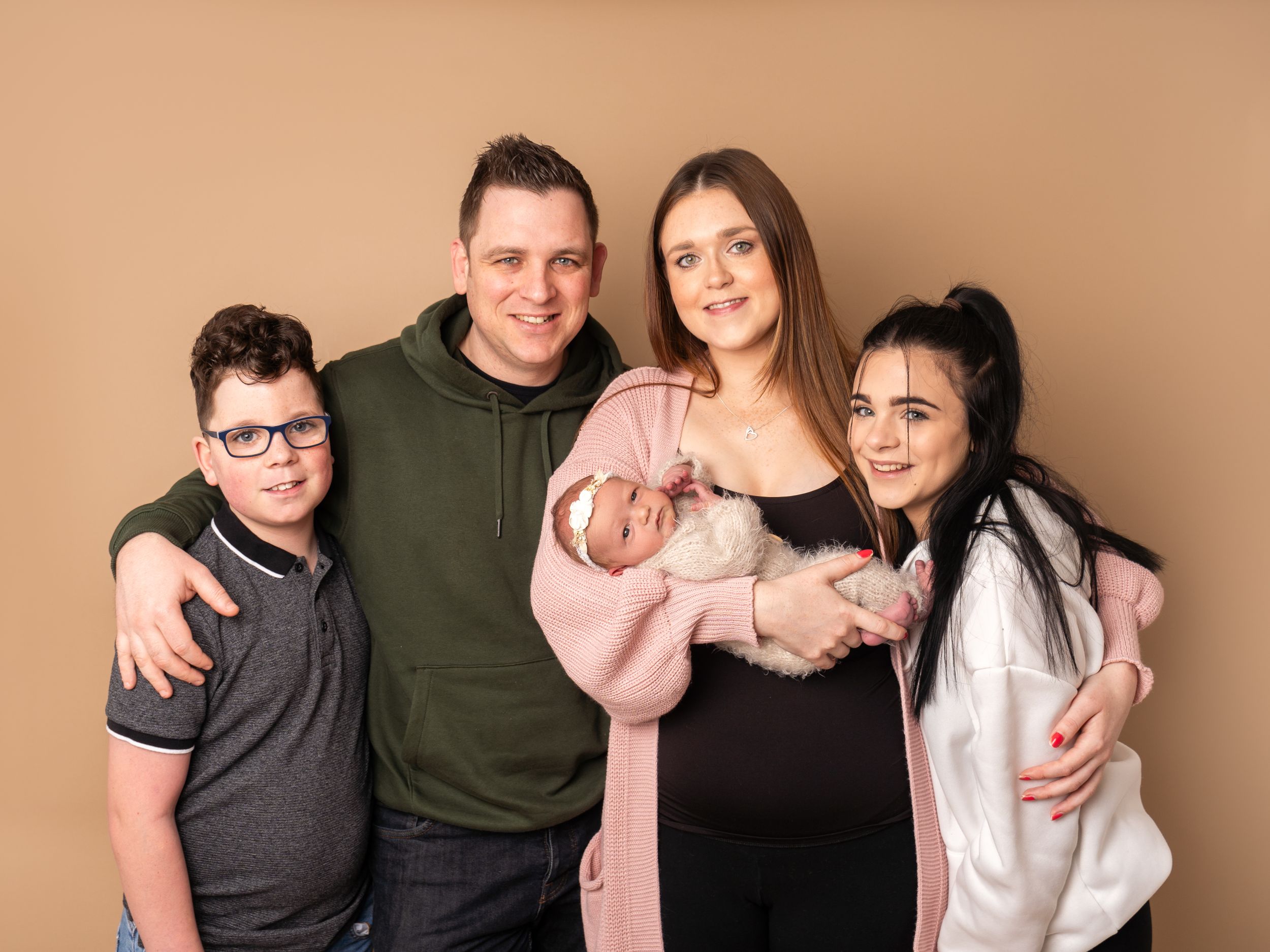 mum holding baby, surrounded by partner and children for portrait photo in studio by family photographer in Doncaster.