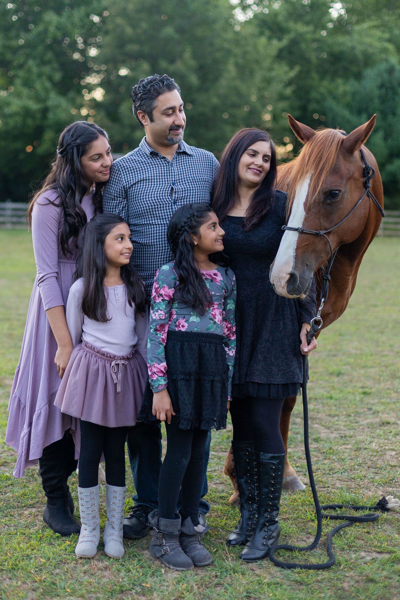 A family poses together with a brown horse in an outdoor field at dusk.